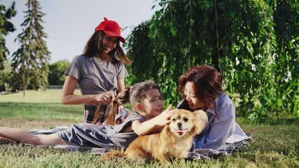 One mother lovingly braids her daughter s hair while the other talks to her. Their daughter pets the long-haired Chihuahua, creating a close family moment in the park
