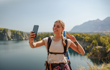 A hiker is enthusiastically taking a selfie with a stunning scenic landscape in the background