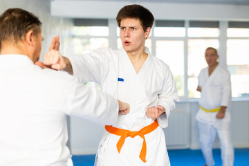 Obraz premium Adult man and young guy in kimono train karate fight in studio