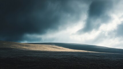 A single ray of sunlight breaks through dark storm clouds to illuminate a grassy hill.