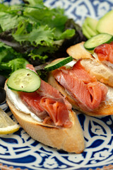 Colorful plate of smoked salmon sandwiches with cucumbers, greens, and olives on a decorative blue platter