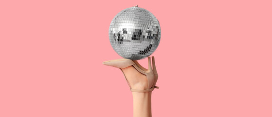 Female legs in high heeled shoes and disco ball on pink background