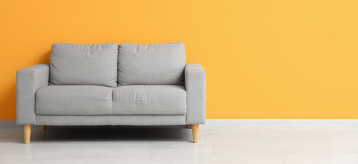 Cozy grey sofa near orange wall in room. Banner for design
