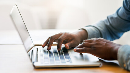 Hands of unrecognizable african american businessman typing on laptop keyboard in office, closeup...