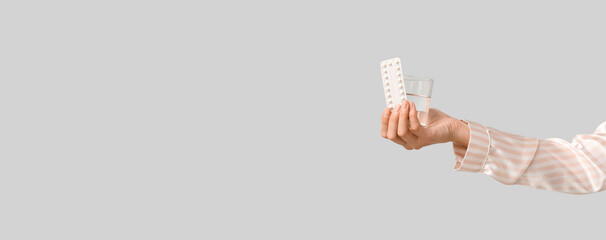 Female hand with birth control pills and glass of water on grey background. Safe sex concept