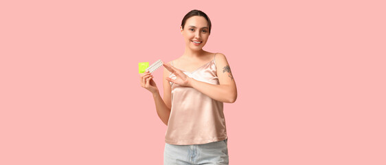 Beautiful young woman with condom and birth control pills on pink background. Safe sex concept
