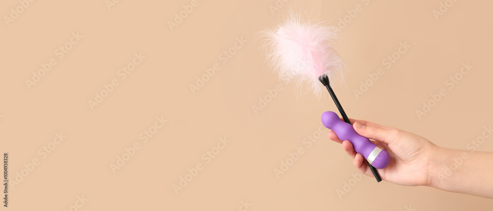 Wall mural female hand with vibrator and feather stick from sex shop on color background, closeup