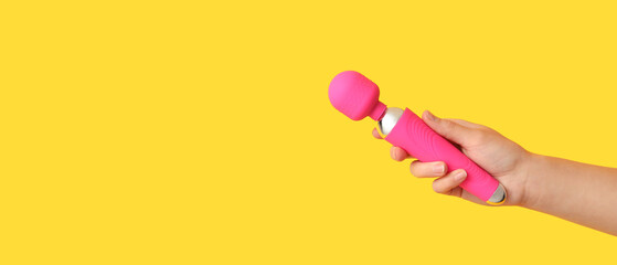Female hand with pink vibrator on yellow background