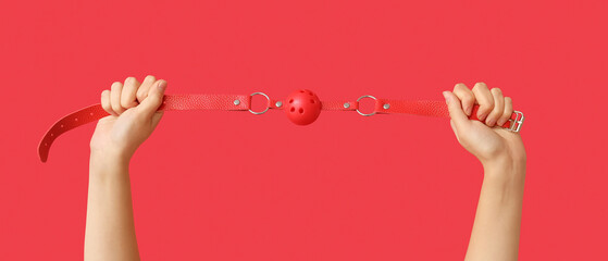 Female hands with mouth gag from sex shop on red background, closeup