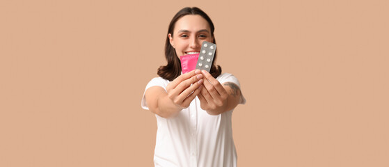 Beautiful young woman with birth control pills and condom on brown background. Safe sex concept