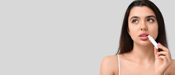 Pretty young woman applying lip balm against grey background with space for text