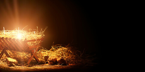 Manger with hay and stones on wooden table against dark background