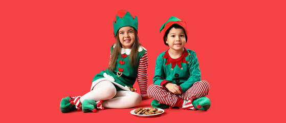 Cute little children dressed as elves with cookies on red background