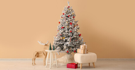 Beautiful Christmas tree with gift boxes and wooden reindeer near beige wall