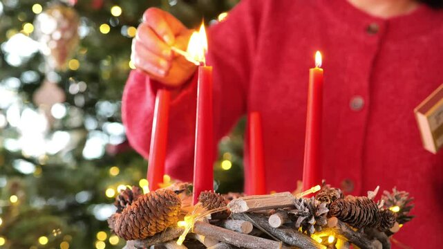 Advent wreath with red candles.Fourth Advent. Fourth week before Christmas. Woman in red sweater lights first candle of Advent wreath on Christmas beautiful tree background.Christmas traditions 