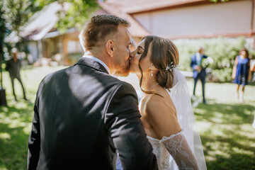 he bride and groom share a kiss during their outdoor wedding ceremony, surrounded by greenery and sunlight in a romantic moment..