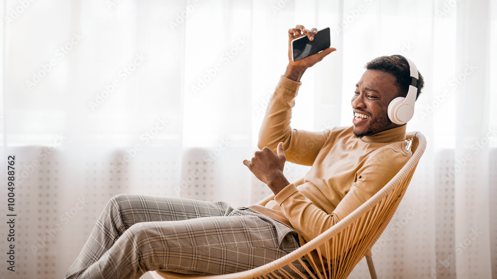 Sticker Positive Afro Man Singing Listening To Music On Smartphone Wearing Wireless Headphones Sitting On Modern Chair Indoor