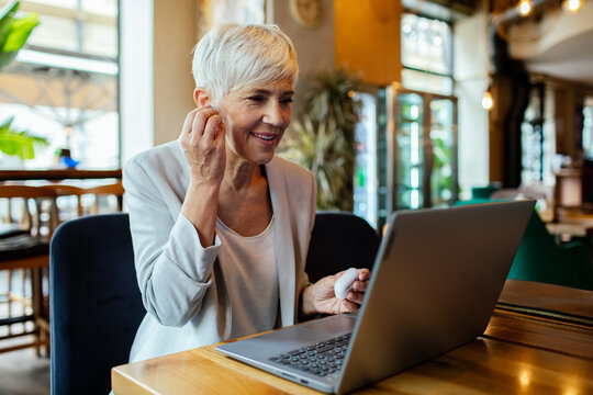 Senior businesswoman working on laptop in a cafe with wireless earbuds