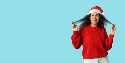 Young African-American woman in Christmas sweater and Santa hat on blue background with space for text