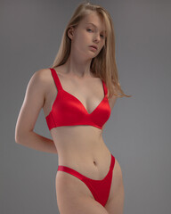 Naklejka premium A model showcases a striking red lingerie set, embodying elegance and poise. The neutral background emphasizes her confident stance and the garment's design.