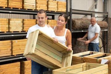 Young male and female customers married couple chooses wooden box in store. Man with wife inspects wooden box for storing garden equipment.