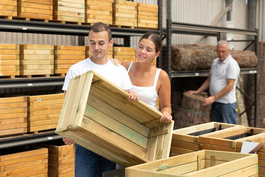 Young male and female customers married couple chooses wooden box in store. Man with wife inspects wooden box for storing garden equipment.