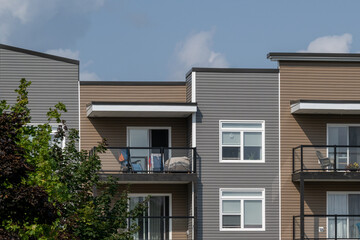 Glass patios on a brown and green colored modern apartment building. Multiple vinyl windows, glass patio doors, and a flat roof. The patios have garden furniture on the decks. 