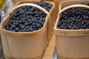 Multiple wood baskets of fresh blueberries. The wild and cultivated berries are blue and purple in color. The large round antioxidants are for sale in bulk at a market. The containers are natural wood