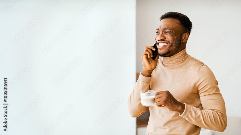 Poster always in touch. smiling black man having phone conversation drinking coffee standing near window in