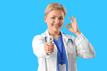 Female medical intern with infrared thermometer on blue background