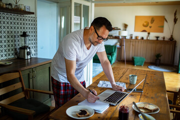 Man reviewing bills and finances on laptop in kitchen