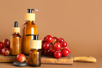 Wooden board with bottles of cosmetic products and ripe grapes on color background