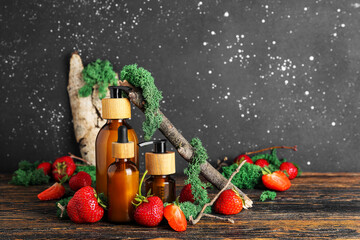 Composition with bottles of cosmetic products, strawberry and moss on wooden table against dark wall