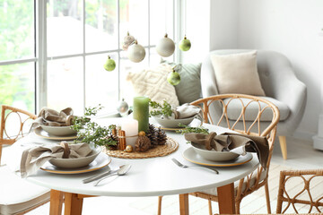 Christmas table setting with hanging balls, burning candles and pine cones in living room