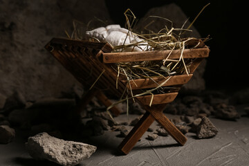Manger with baby, hay and stones on dark table
