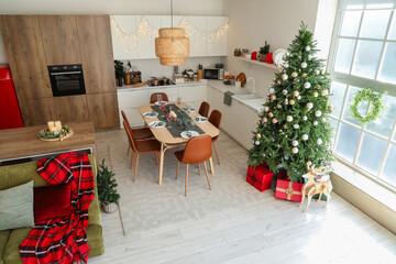 Interior of festive kitchen with Christmas tree, green sofa and served dining table