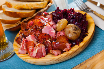 Sliced baked pork shank served with vegetable garnish of braised red cabbage on wooden board..