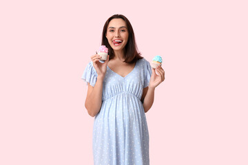 Beautiful happy pregnant woman with delicious cupcakes on pink background. Gender reveal party...