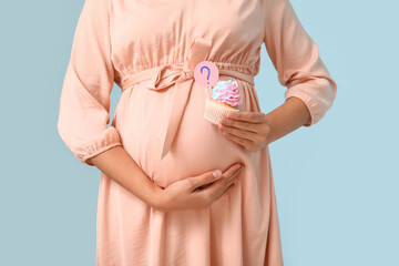 Beautiful pregnant woman with delicious cupcake and question mark on blue background, closeup....
