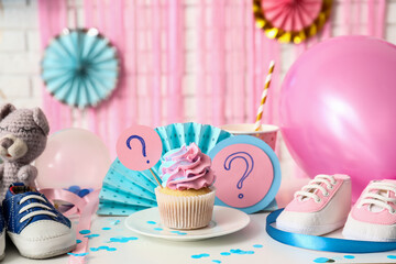 Delicious cupcake with question marks, baby booties and decorations on table against white brick...