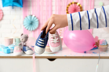 Female hand with baby booties and decorations on table against white brick background. Gender...