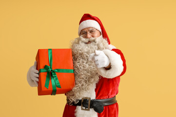 Santa Claus with Christmas gift pointing at viewer on yellow background