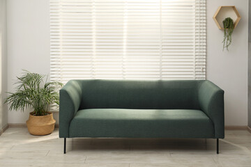 Comfortable couch and green plants near light wall indoors. Interior design