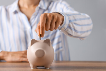 Woman putting coin into piggy bank at wooden table, closeup