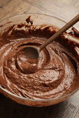 Chocolate dough in bowl and spoon on wooden table, closeup