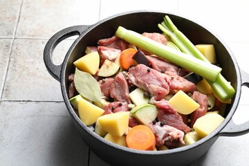 Cooking stew. Uncooked meat and vegetables in pot on white tiled table
