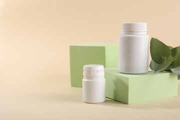Plastic medical bottles, eucalyptus leaves and podiums on beige background, space for text