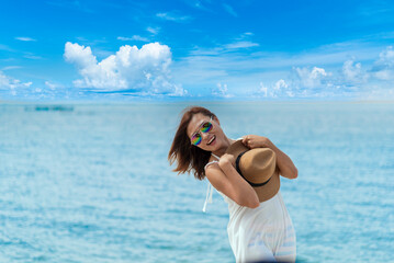 Cheerful asian woman barefoot walking on tropical summer beach. Woman walking along wave of sea water and sand on the beach. Enjoyment barefoot walk outdoor with freedom. Relaxation Travel Concept.