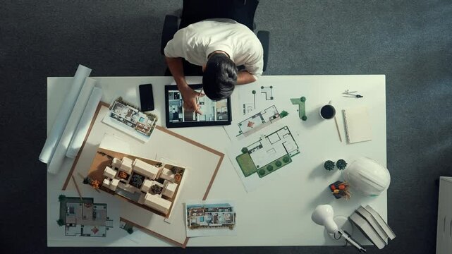 Top view of business man using tablet plan house design while sitting at meeting table with blueprint and equipment scatter around. Aerial view of civil engineer working at blueprint. Alimentation.