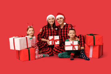 Happy family in pajamas with Christmas gifts on red background